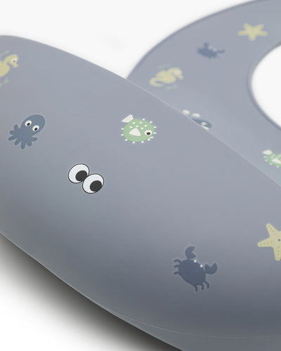 A  closeup of our soft silicone bib in dusty blue color with small see animal illustrations and an adjustable neck strap.