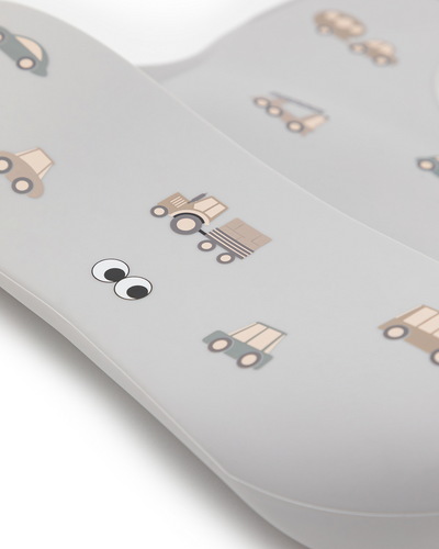 A close up of our silicone bib with a pattern of small cute cars and trucks. Adjustable strap in the neck and an extra large cup to catch food an fluids.