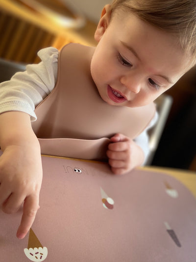 A child wearing our silicone bib in old rose color with an adjustable neck strap and a extra large cup  to catch food and fluids.