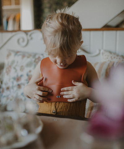 Child sitting at the table with our Placemat in old rose color wearing a silicone bib.
