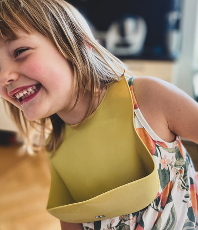 A child wearing our dusty lemon silicone bib with an extra big cup and adjustable fitting.
