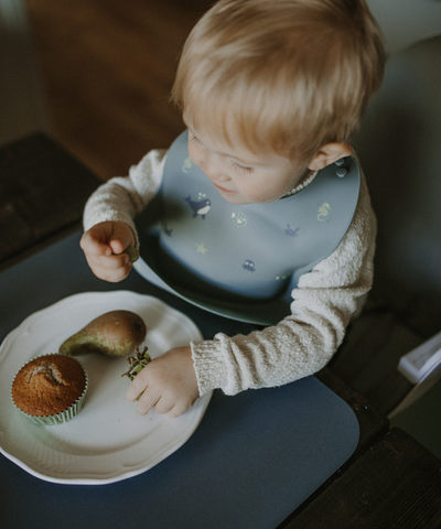 A child wearing our soft silicone bib in dusty blue color with small see animal illustrations and an adjustable neck strap.